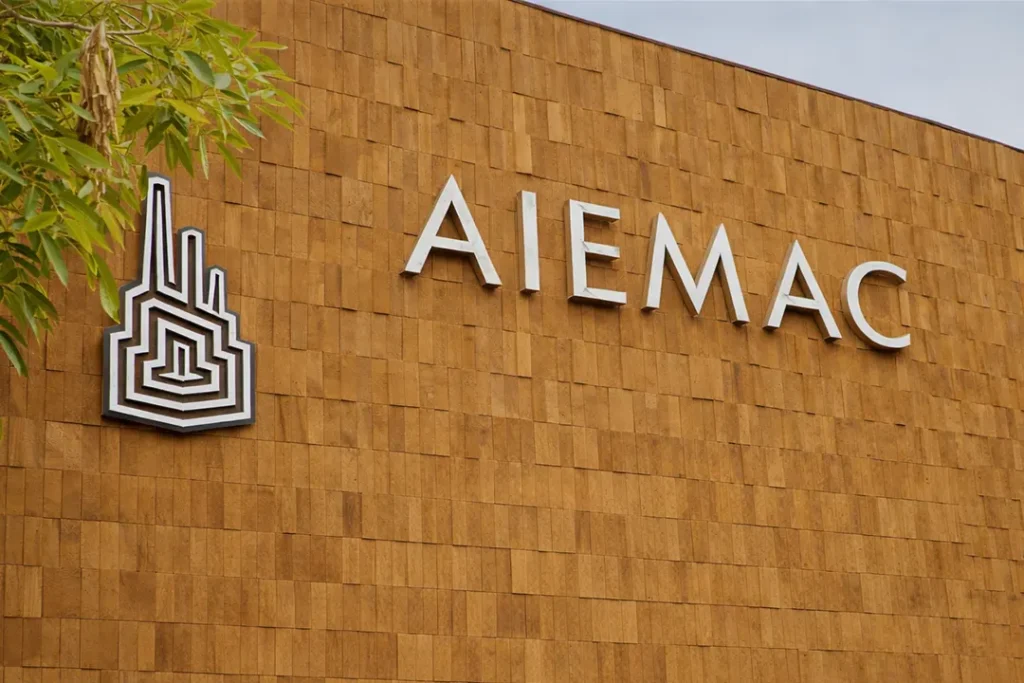 Fachada del edificio de AIEMAC con logotipo y letras metálicas sobre muro